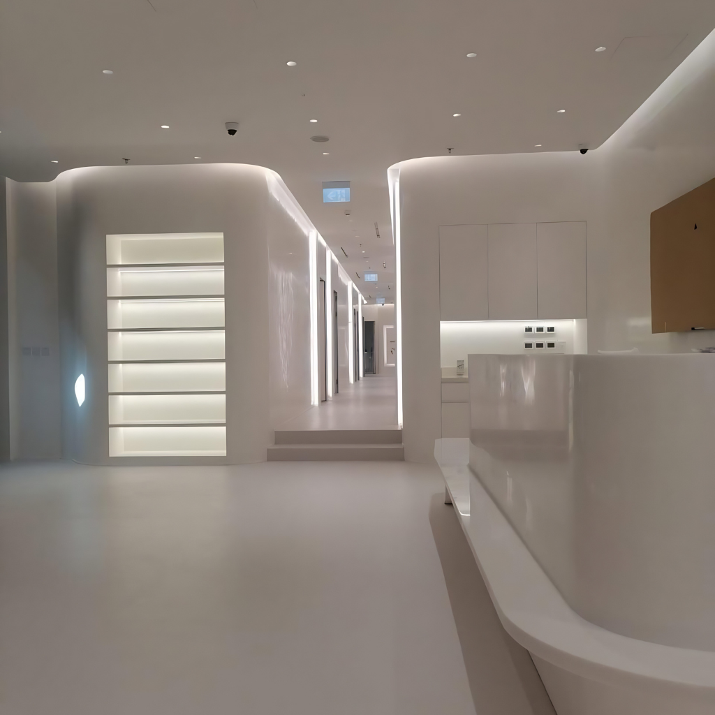 Ultra-modern white interior with curved walls, backlit shelving on the left, and a white reception desk on the right; hallway recedes into the distance despite soft ambient lighting.
