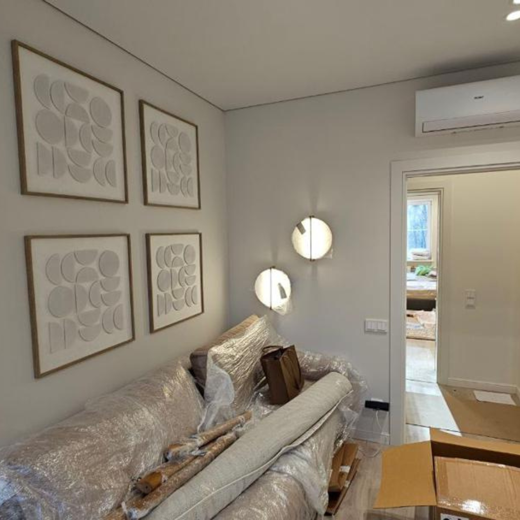 Living room with light gray walls, four framed abstract circle artworks, and a sofa covered in plastic with packing materials and boxes nearby.