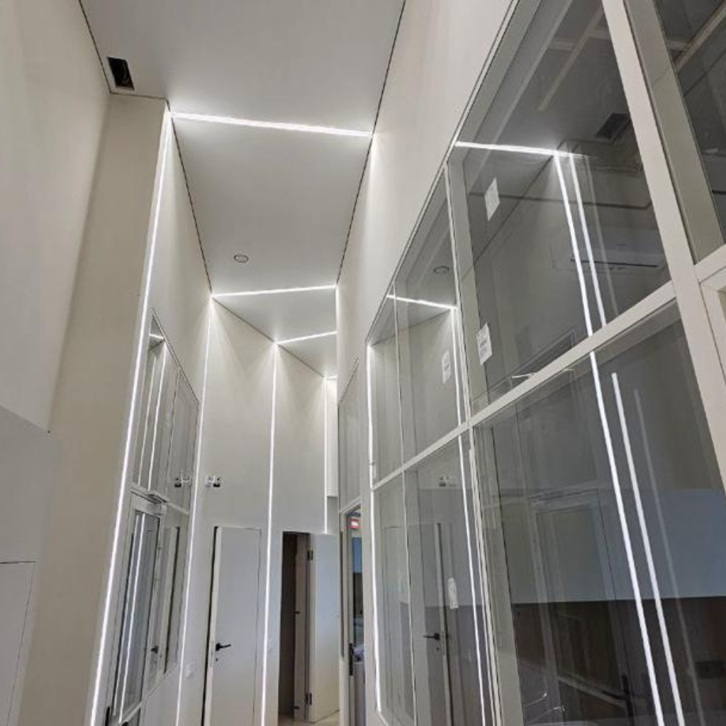 Modern white hallway with glass walls and recessed LED strip lighting along edges.