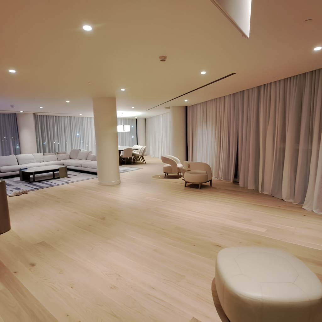 Spacious modern lounge with pale wood floor, white sectional sofa, and round cream chairs under soft ceiling lights.