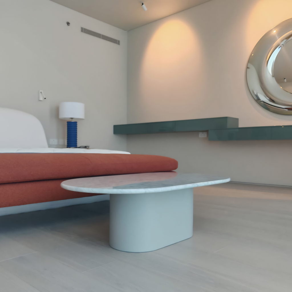 Modern hotel suite living area with round marble coffee table, orange sofa, and a large circular wall mirror.